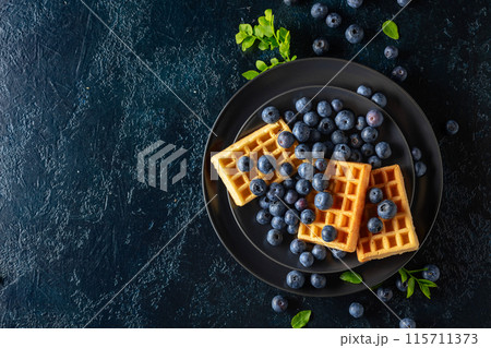 Belgian waffles with blueberries on a black plate. 115711373