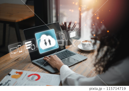 A person working on a laptop with cloud backup icons, symbolizing data security and storage solutions in a contemporary office setting. 115714719