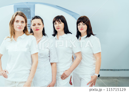 Four women in white shirts stand in row in front of a machine. They are all wearing white uniforms and appear to be nurses. Concept of professionalism and teamwork Four women in white shirts stand in row in front of a machine. They are all wearing white uniforms and appear to be nurses. Concept of professionalism and teamwork 115715129