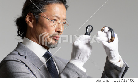 腕時計をルーペで確認する男性鑑定士 腕時計をルーペで確認する男性鑑定士 115715400