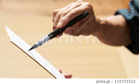 筆ペンで短冊に文字を書く男性の手元 115715512