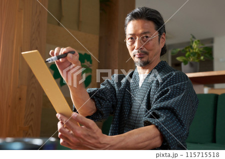 短冊に文字を書く和服の男性 115715518