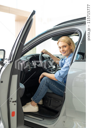 Blonde woman in a blue shirt sitting in a car and looking contented Blonde woman in a blue shirt sitting in a car and looking contented 115715777