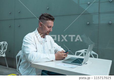 Young Caucasian male passenger in stylish casual clothes using smartphone and laptop keyboard, sit has training online meeting on laptop computer in airline lounge wait transit international airport Young Caucasian male passenger in stylish casual clothes using smartphone and laptop keyboard, sit has training online meeting on laptop computer in airline lounge wait transit international airport 115717025