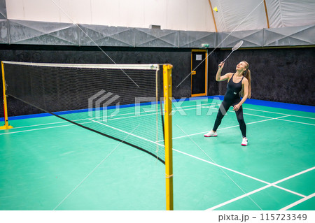 Sports young woman with racket and shuttlecock is exercising, playing in badminton on inside court Sports young woman with racket and shuttlecock is exercising, playing in badminton on inside court 115723349