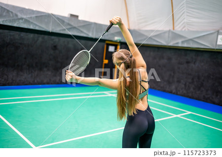 Sports young woman with racket and shuttlecock is exercising, doing warm-up before playing in badminton on inside court Sports young woman with racket and shuttlecock is exercising, doing warm-up before playing in badminton on inside court 115723373