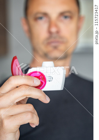 Close up view of man using medicine dry powder inhaler for treatment asthma or COPD diseases. Pharmaceutical product is used to treat lung inflammation and prevent asthma attack. Close up view of man using medicine dry powder inhaler for treatment asthma or COPD diseases. Pharmaceutical product is used to treat lung inflammation and prevent asthma attack. 115723417