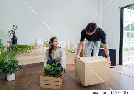 Young Couple Moving into New House, Unpacking Boxes and Arranging Plants in Modern Living Room 115724850