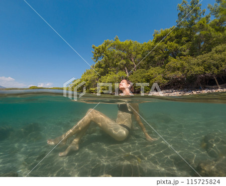 Young female on holidays enjoy floating on a crystal clear water beach of Antalya Turkey. Asian beautiful woman swimming with open arms. Relax and tranquility. Travel and Holiday concept. 115725824