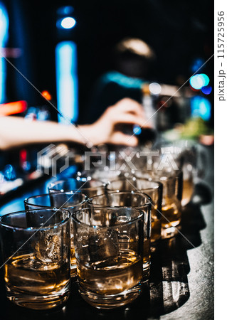 Bartender Preparing Multiple Whiskey Cocktails at a Busy Bar 115725956