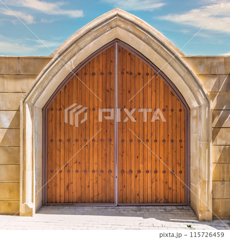 Pair of wooden doors with decorative metal accents are set within a stone archway Pair of wooden doors with decorative metal accents are set within a stone archway 115726459