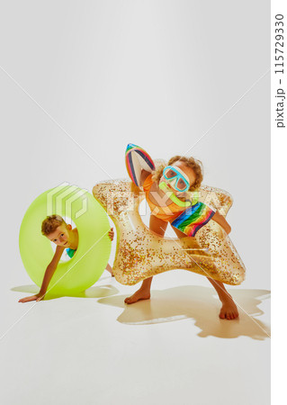 Little children, boy and girl in swimwear and diving masks have fun with pool floats ready to swim against white studio background. Little children, boy and girl in swimwear and diving masks have fun with pool floats ready to swim against white studio background. 115729330