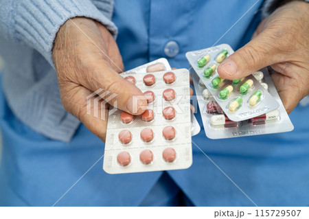 Asian senior woman patient holding antibiotics capsule pills  for treatment infection patient in hospital, Pharmacy drugstore concept. 115729507