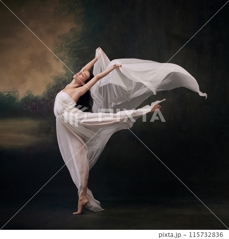 Dancer's leap highlighted by gentle flow of her gown, creating image of aerial grace against vintage studio background. 115732836