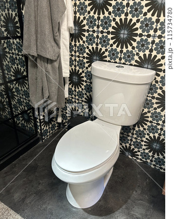 A modern bathroom features a white toilet, patterned tile wall, and hanging towels 115734780