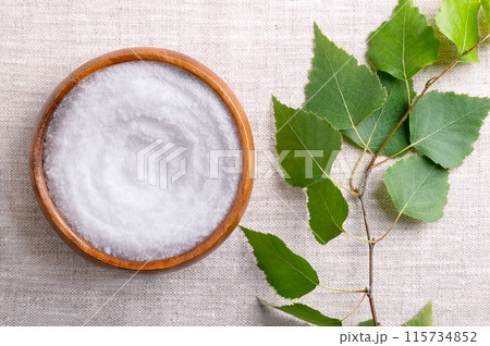 Birch sugar, table sweetener based on xylitol, in a wooden bowl on linen fabric. Also called xylite, a sugar substitute of natural origin with 40 percent fewer calories. A birch branch on the left. 115734852