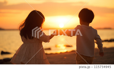 夕日をバックに海辺の砂浜で手を繋ぐ小さい男の子と女の子の後ろ姿 115734945