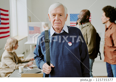 Medium portrait of senior Caucasian male citizen with pin on sweater standing at polling station looking at camera 115735377