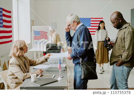 Side view shot of senior Caucasian man attending polling place taking ballot paper to vote on election day 115735378