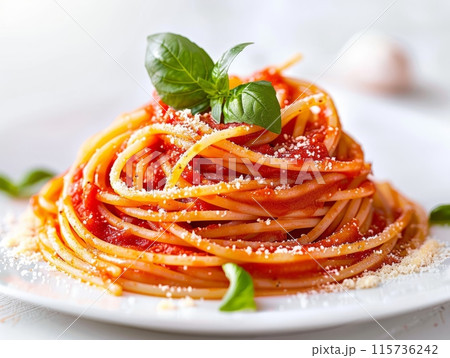 A gourmet serving of spaghetti topped with fresh tomato chunks and a basil leaf, elegantly presented in a white dish. A gourmet serving of spaghetti topped with fresh tomato chunks and a basil leaf, elegantly presented in a white dish. 115736242