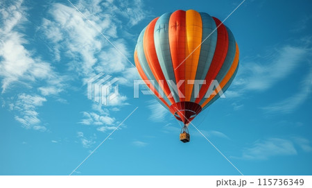 Vibrant hot air balloon floating in a clear blue sky with fluffy white clouds. 115736349