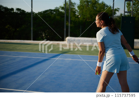 Female tennis player preparing to serve on outdoor court Female tennis player preparing to serve on outdoor court 115737595