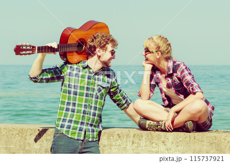 Young man playing guitar to his girlfriend by seaside 115737921