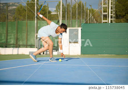 Female tennis player reaching for ball on outdoor court Female tennis player reaching for ball on outdoor court 115738045