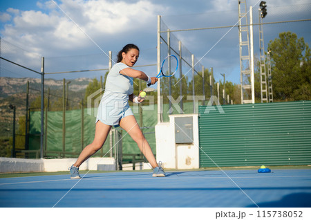 Female tennis player practicing on outdoor court under blue sky Female tennis player practicing on outdoor court under blue sky 115738052