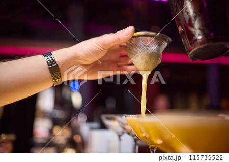Bartender pours pink cocktail into martini glass with flair Bartender pours pink cocktail into martini glass with flair 115739522