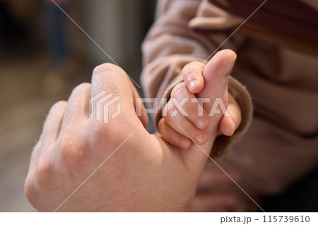 A close up of a persons thumb touching a baby tiny finger 115739610