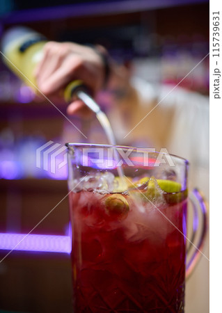 Bartender pours pink cocktail into martini glass with flair 115739631