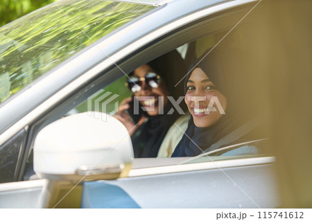 Two Muslim women wearing hijab converse on a smartphone while traveling together in a car through the  115741612