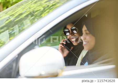 Two Muslim women wearing hijab converse on a smartphone while traveling together in a car through the  115741620