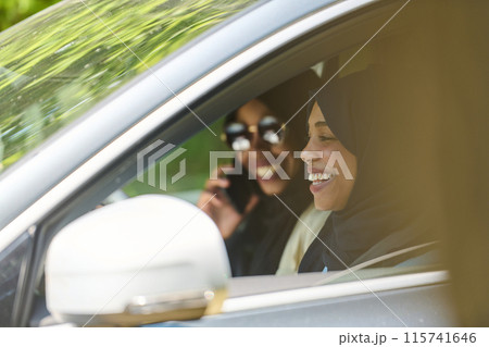 Two Muslim women wearing hijab converse on a smartphone while traveling together in a car through the Two Muslim women wearing hijab converse on a smartphone while traveling together in a car through the 115741646
