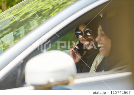 Two Muslim women wearing hijab converse on a smartphone while traveling together in a car through the Two Muslim women wearing hijab converse on a smartphone while traveling together in a car through the 115741667