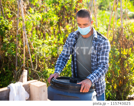 Male worker in mask arranging garden barrel 115743025