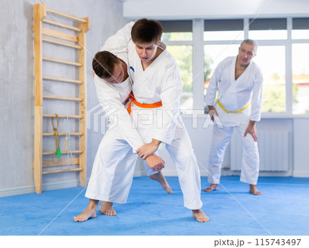 Two men practice grabbing and throwing sports mats during judo training under the guidance of an experienced mature coach Two men practice grabbing and throwing sports mats during judo training under the guidance of an experienced mature coach 115743497