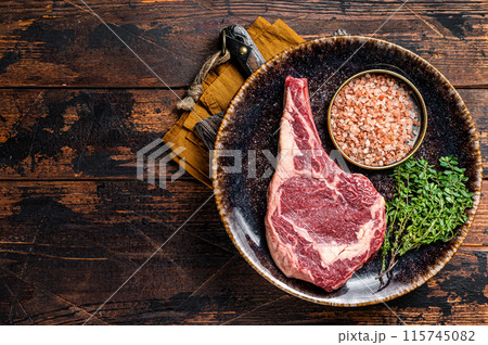Raw prime cowboy or rib eye steak, dry aged beef meat. Wooden background. Top view. Copy space 115745082