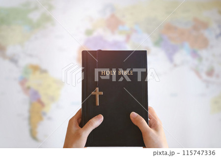 Christian holding the holy cross of Jesus Christ and the Bible in his hands and praying for missions, gospel and evangelism, world map background Christian holding the holy cross of Jesus Christ and the Bible in his hands and praying for missions, gospel and evangelism, world map background 115747336