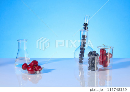 On both sides of the countertop displaying some lab items consist of beaker, boiling flask, test tube, erlenmeyer flask and erlenmeyer with fresh fruits as cherry and blueberry, over blue background On both sides of the countertop displaying some lab items consist of beaker, boiling flask, test tube, erlenmeyer flask and erlenmeyer with fresh fruits as cherry and blueberry, over blue background 115748389