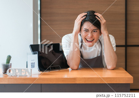 頭を抱えるカフェオーナーの若いアジア人男性（倒産・しくじり・ローン・潰れる・絶望） 115752211