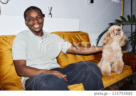 Minimal portrait of young African American man sitting on velvet couch with cute dog and smiling happily at camera, copy space Minimal portrait of young African American man sitting on velvet couch with cute dog and smiling happily at camera, copy space 115753085