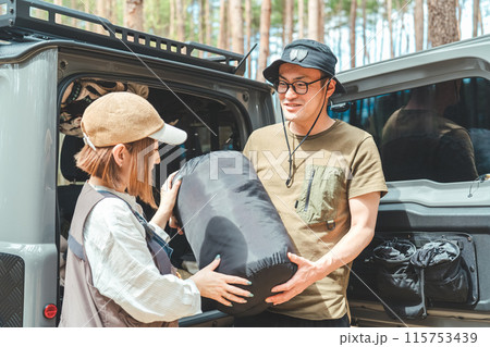 オートキャンプ場で荷物・寝袋を運ぶアウトドア好きな夫婦キャンパー（到着・RV車・SUV・自動車） 115753439