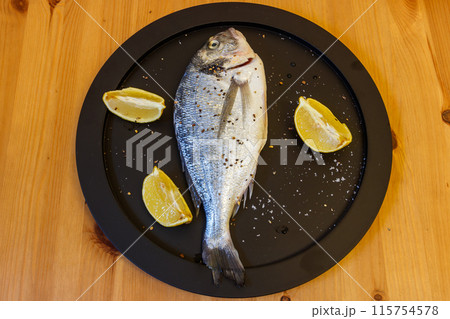 Raw fresh fish dorado with lemon and spices on wooden table. Top view Raw fresh fish dorado with lemon and spices on wooden table. Top view 115754578