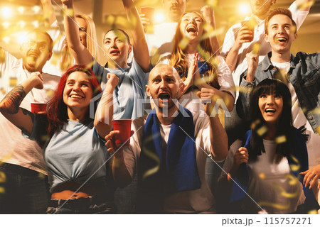 Crowd of sport fans cheering during match on stadium. Excited people standing raised arms , clapping and yelling to encourage their team 115757271