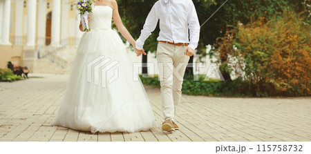 Wedding couple, bride in white dress and groom in shirt holding hands walking in summer park Wedding couple, bride in white dress and groom in shirt holding hands walking in summer park 115758732