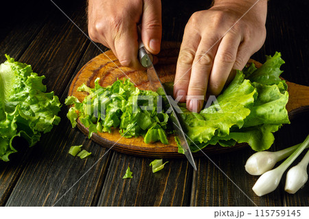Chef cutting lettuce leaves on wooden board with knife in hand before preparing tasty breakfast. Vegetable diet concept 115759145
