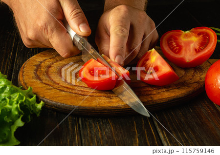 A chef cuts a ripe tomato on a wooden board with a knife in his hands before preparing a delicious breakfast. Tomatoes diet concept 115759146