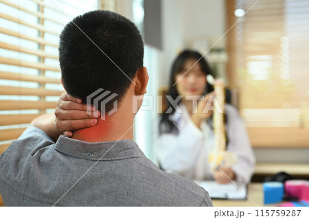 Male patient touching painful neck near explaining to physiotherapist about his pain in consulting room 115759287
